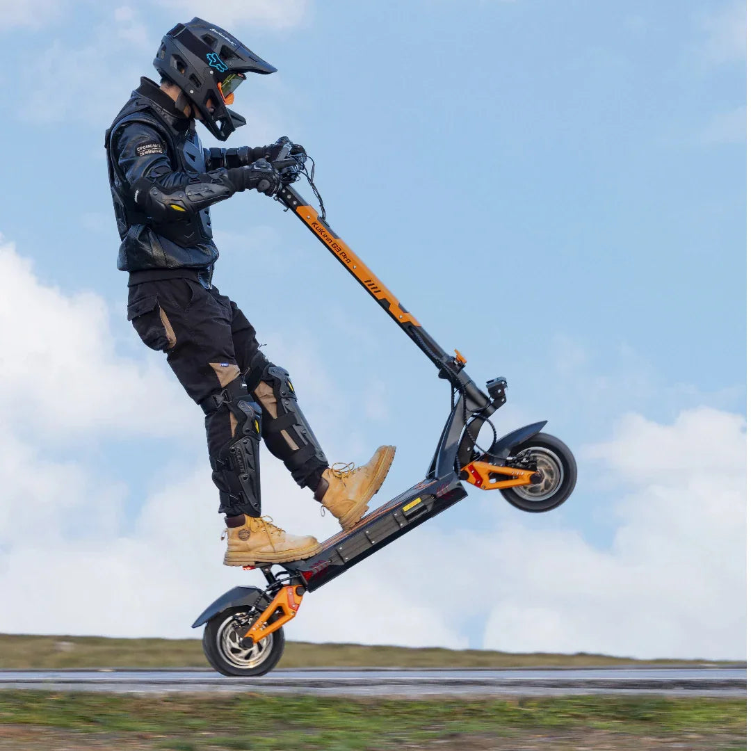 Rider performing stunt on black and orange electric scooter mid-air against blue sky