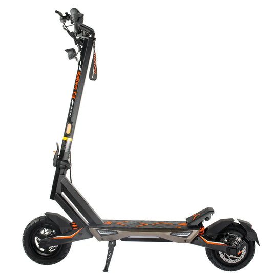 Black and orange electric scooter with off-road tires and front headlight, standing upright on kickstand