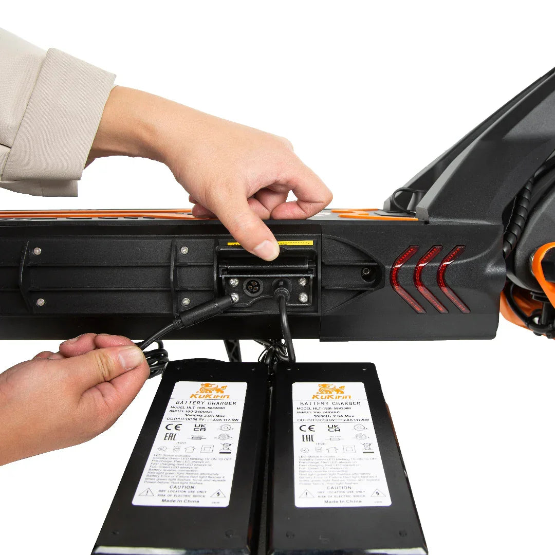 Hand plugging charger into electric scooter battery port with dual chargers labeled KUKiin