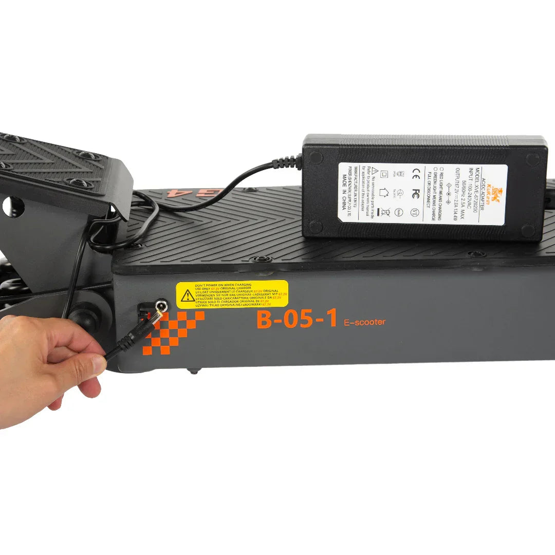 Hand plugging charger into B-05-1 e-scooter with orange checkered decal and safety label