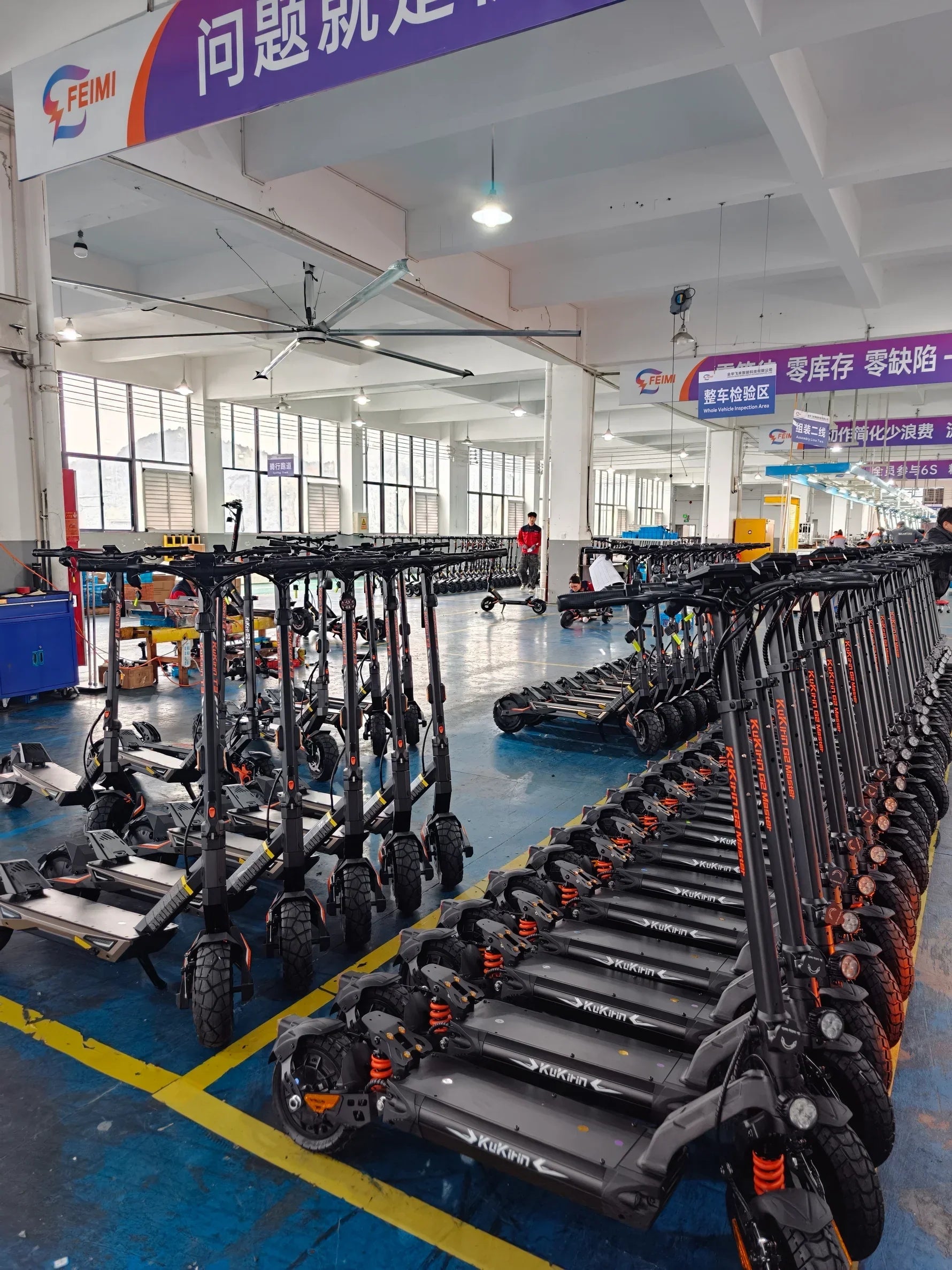Rows of KuKihn electric scooters in a factory assembly area, ready for inspection and shipping.