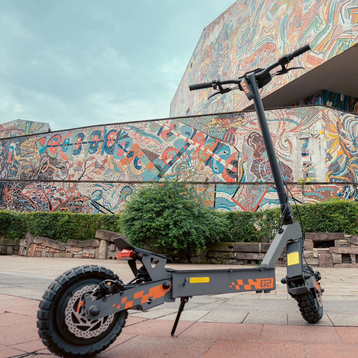 G2 electric scooter with fat tires parked on pavement near colorful mosaic wall